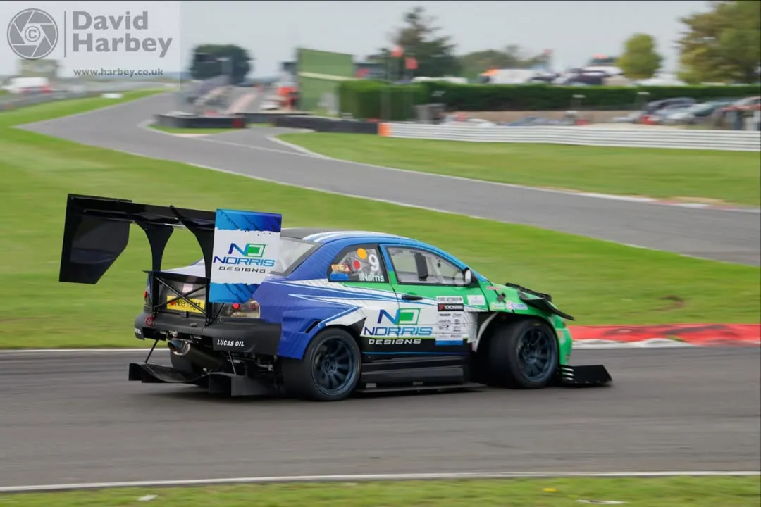 Blue and green race car with large rear wing driving on a curved racetrack.